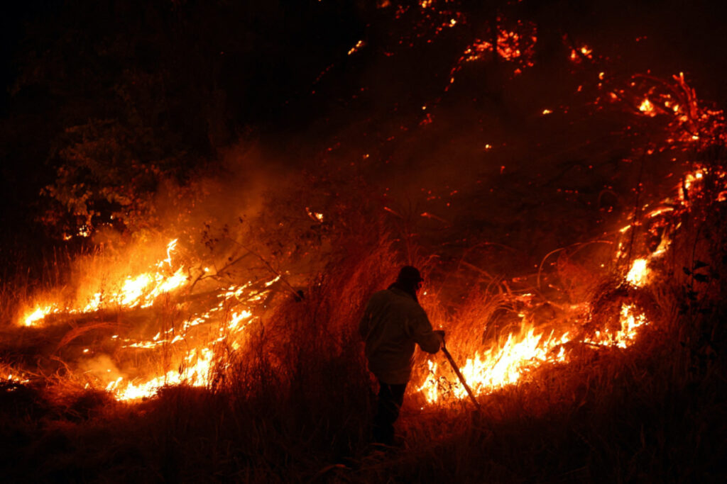 A local resident works to extinguish a wildfire in Nacimiento, Chile, February 7, 2023. REUTERS/Ivan Alvarado