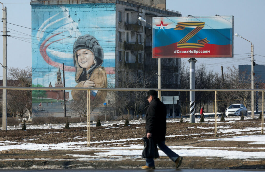 FILE PHOTO: A pedestrian walks near a board, which displays the symbol "Z" in support of the Russian armed forces involved in the country's military campaign in Ukraine, in the settlement of Chernomorskoye, Crimea, February 11, 2023. A sign on the board reads: "We don't abandon our people". REUTERS/Alexey Pavlishak