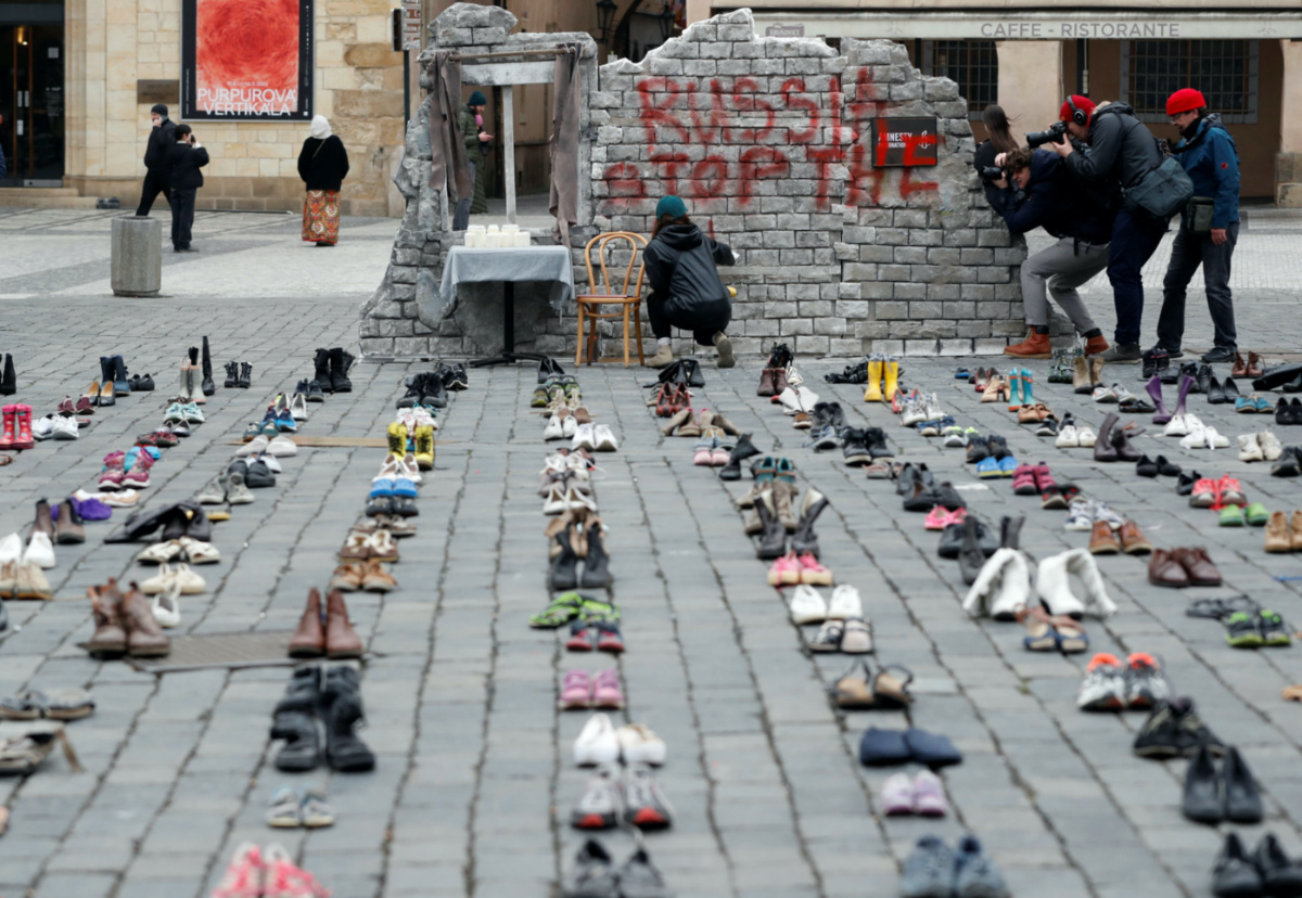 A woman sprays a sign next to the shoes symbolising war crimes committed against Ukrainian civilians at the Old Town Square to mark the one-year anniversary of the Russian invasion of Ukraine, in Prague, Czech Republic February 15, 2023. 