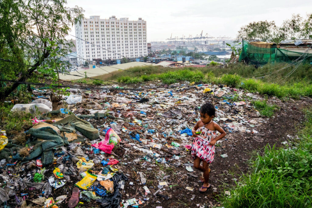 FILE PHOTO: A girl walks past plastic waste dumped at a former landfill in Manila, Philippines, May 27, 2022. REUTERS/Lisa Marie David