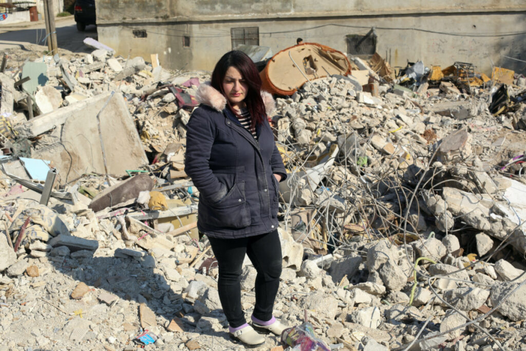 Um Kanan, a Syrian woman who survived the quake along with her children, stands on the rubble of what was once her building, in the aftermath of a deadly earthquake, in Jableh, Syria February 14, 2023.