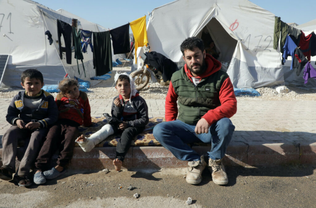 Displaced Syrian man, Omar Barakat, sits next to an injured child at a camp for earthquake survivors, on the outskirts of rebel-held town of Jandaris, Syria February 17, 2023.