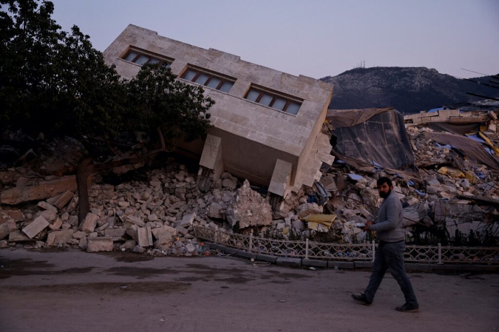 FILE PHOTO: A man walks by a collapsed building and rubble, in the aftermath of a deadly earthquake, in Antakya, Hatay province, Turkey, February 21, 2023.