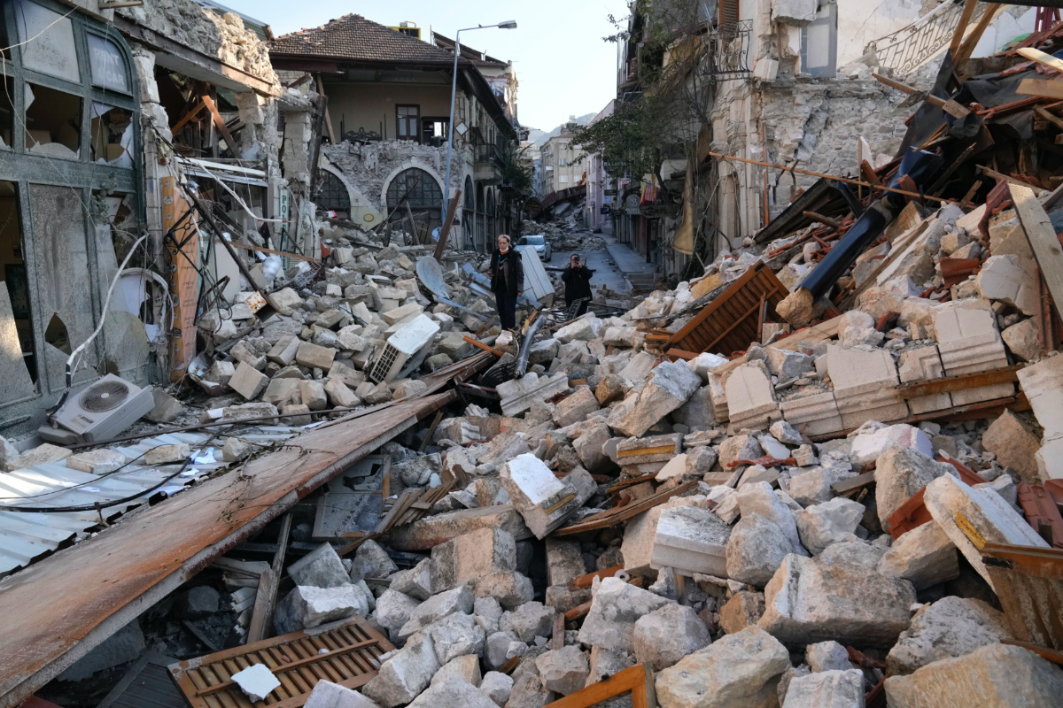 A Turkish woman stands on the debris of heritage houses that destroyed during the devastated earthquake, in the old city of Antakya, southern Turkey, Monday, Feb. 13, 2023