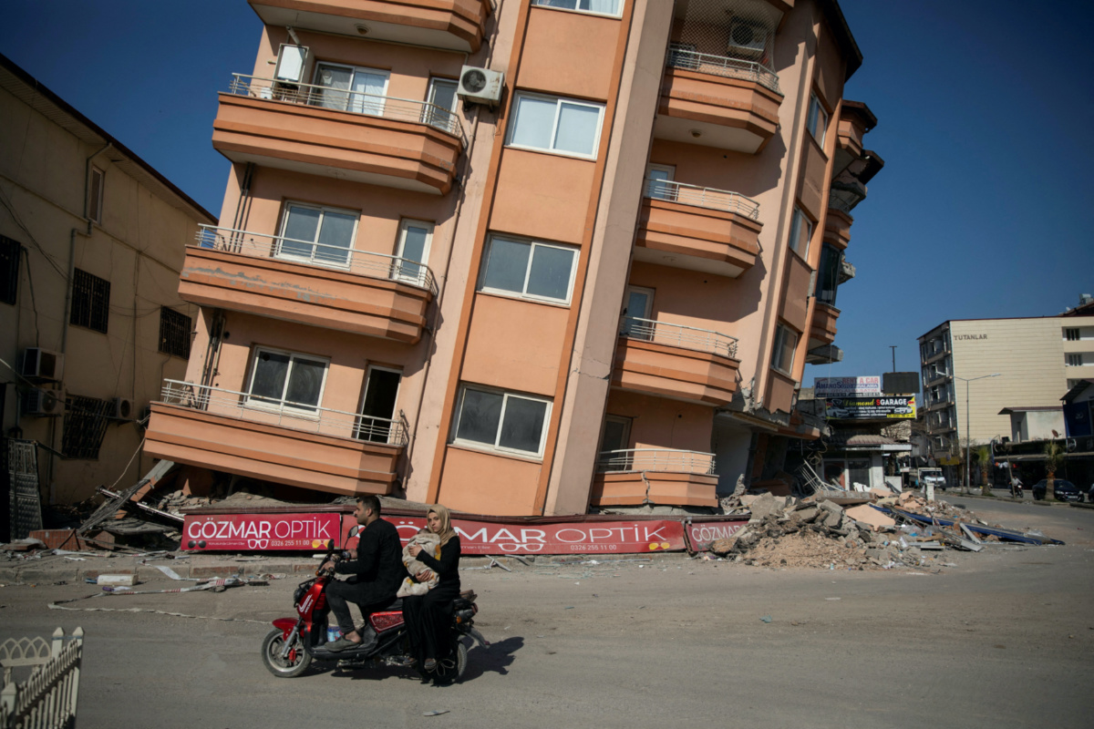 A man and a woman holding a baby ride a scooter past a destroyed building in the aftermath of the deadly earthquake in Kirikhan, Hatay province, Turkey, February 18, 2023.