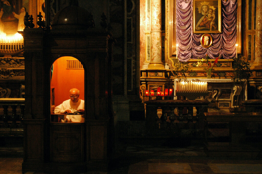 A priest reads inside a confessional.