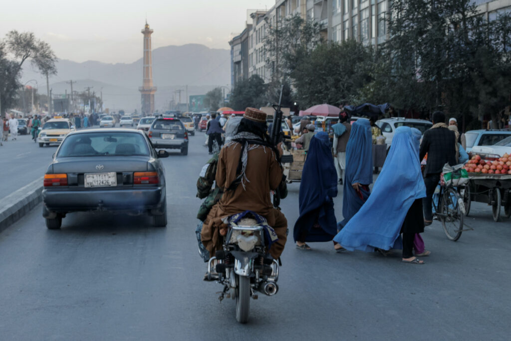 FILE PHOTO: A group of women wearing burqas crosses the street as members of the Taliban drive past in Kabul, Afghanistan October 9, 2021. REUTERS/Jorge Silva