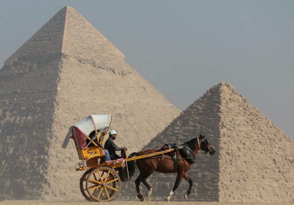 Tourists ride a horse-drawn cart in front of the Great Pyramids plateau in Giza, Egypt December 11, 2022.