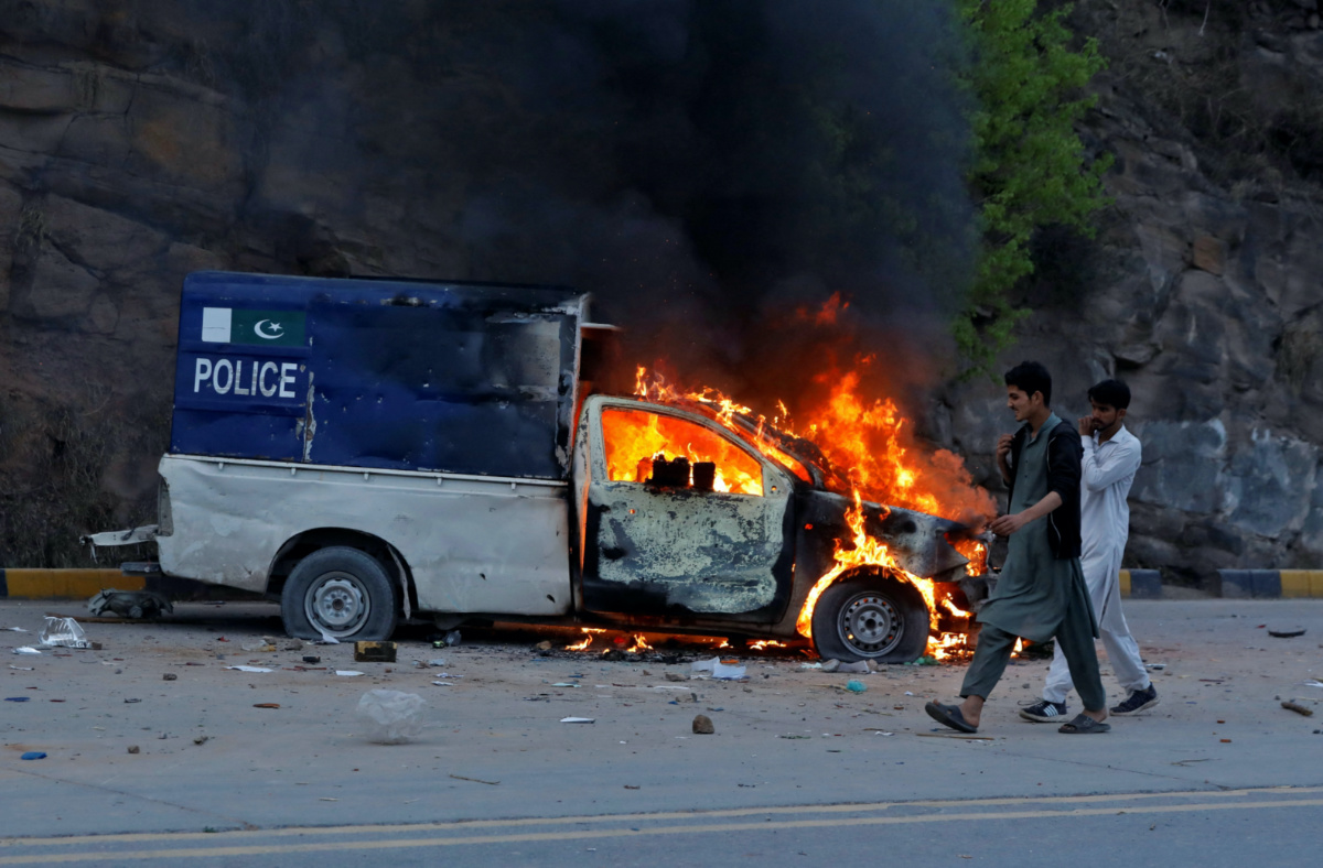 Men walk past a burning police vehicle during clashes between the supporters of former Pakistani Prime Minister Imran Khan and police in Islamabad, Pakistan, March 18, 2023. REUTERS/Fayaz Aziz