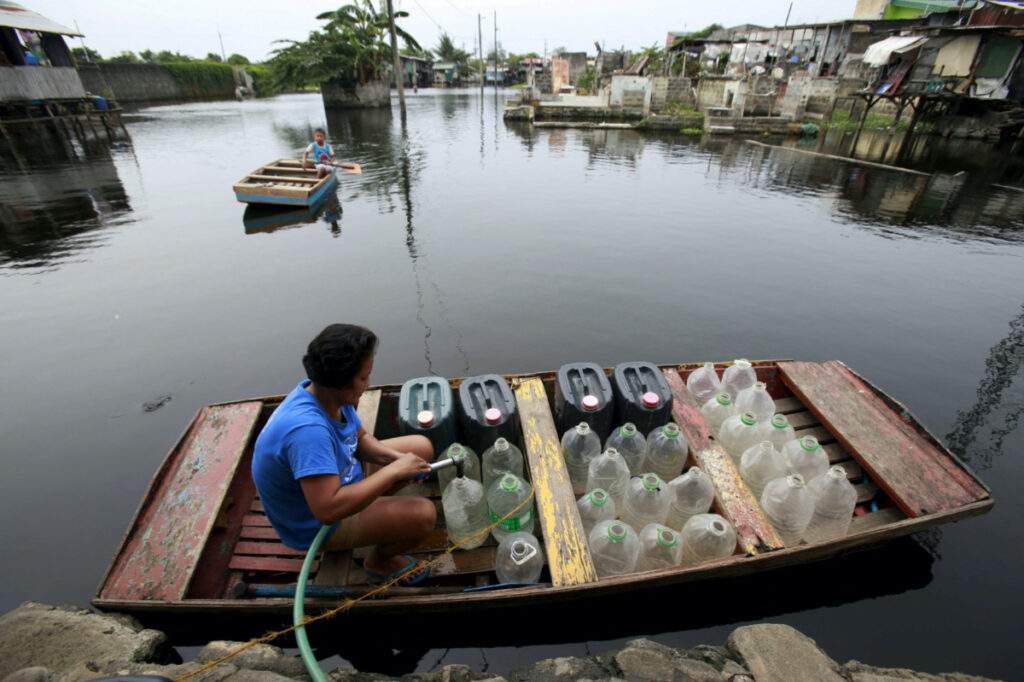 A resident living in a flooded area refills plastic containers with drinking water on an improvised "banca" in Artex compound, Malabon city, north of Manila, Philippines March 4, 2016.