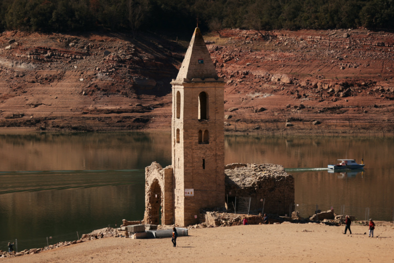 Tourists walk while fishermen collect fish from the Sau reservoir next to a church of the village of San Roman de Sau after its re-emerging as Sau reservoir has lowest level since 1990 due to extreme drought in Catalonia, near Vic, Spain, on 15th March 15, 2023. 