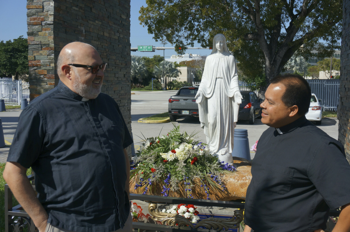 The Rev. Marcos Somarriba, left, pastor of St. Agatha Catholic Church, and the Rev. Elvis González, pastor of St. Michael Catholic Church, talk in front of a statue of the Virgin Mary on the campus of St. Agatha, Monday, Feb. 20, 2023 in Miami. The two Catholic priests, originally from Nicaragua, have been helping those fleeing the Central American country and settling in the Miami area by connecting them with legal, housing and humanitarian resources. (AP Photo/Giovanna Dell'Orto