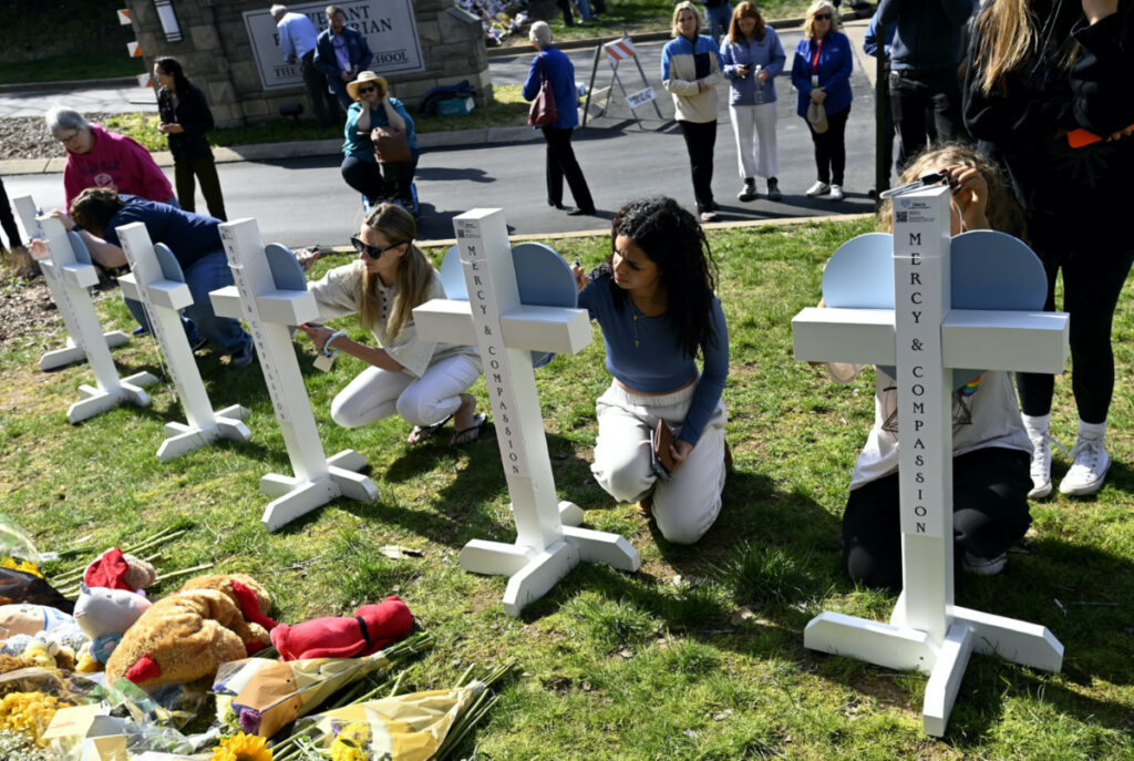 People gather to sign wooden crosses placed at a makeshift memorial by the entrance of The Covenant School, on Tuesday, 28th March, 2023, in Nashville, Tennessee.
