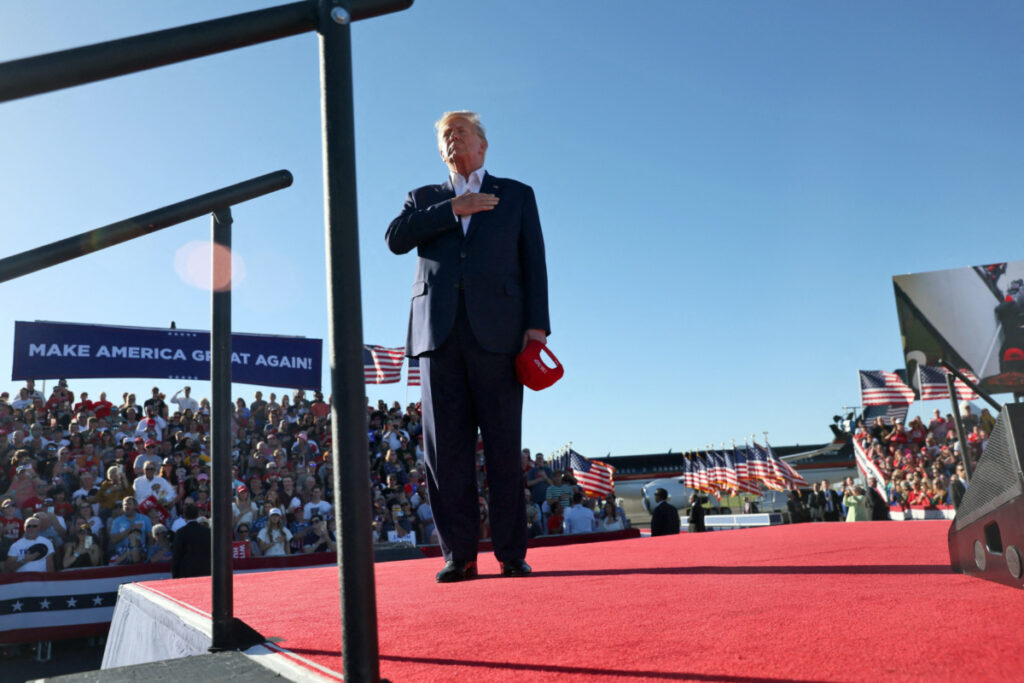 Former US President Donald Trump listens to a choir of people incarcerated due to their actions on 6th January sing The Star-Spangled Banner, as footage from 6th January plays on a screen behind him, during the first rally for his re-election campaign at Waco Regional Airport in Waco, Texas, US, on 25th March, 2023.