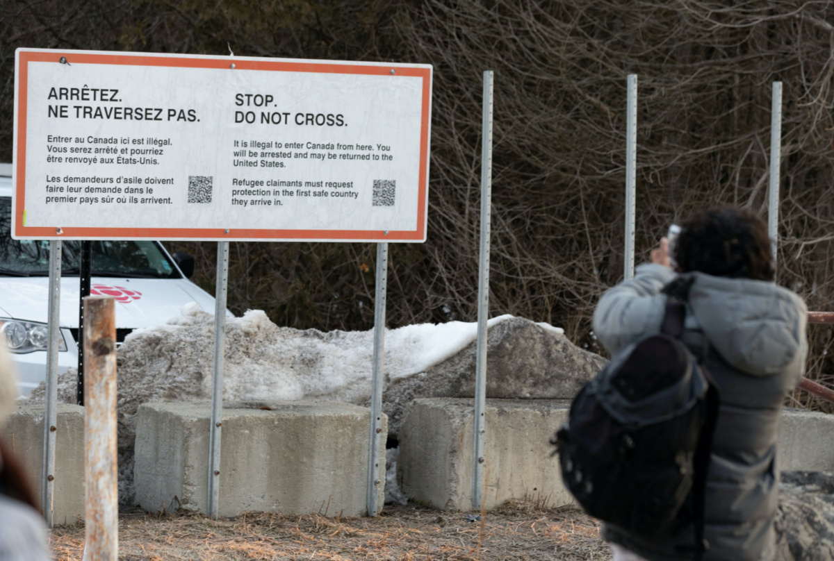 A migrant takes a photo of a new border sign before deciding to cross into Canada at Roxham Road, an unofficial crossing point from New York State to Quebec for asylum seekers, in Champlain, New York, U.S. March 25, 2023. REUTERS/Christinne Muschi