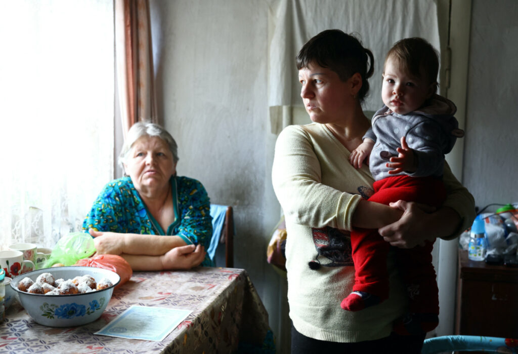 Natalia Lukina looks out the window as she holds her baby Kateryna, who was born during the Russian occupation, next to her mother Olha inside their house just 1.5 kilometers away from Russian positions across the Dnipro river, amid Russia's invasion of Ukraine, in Antonivka, Kherson region, Ukraine, February 23, 2023. REUTERS/Lisi Niesner
