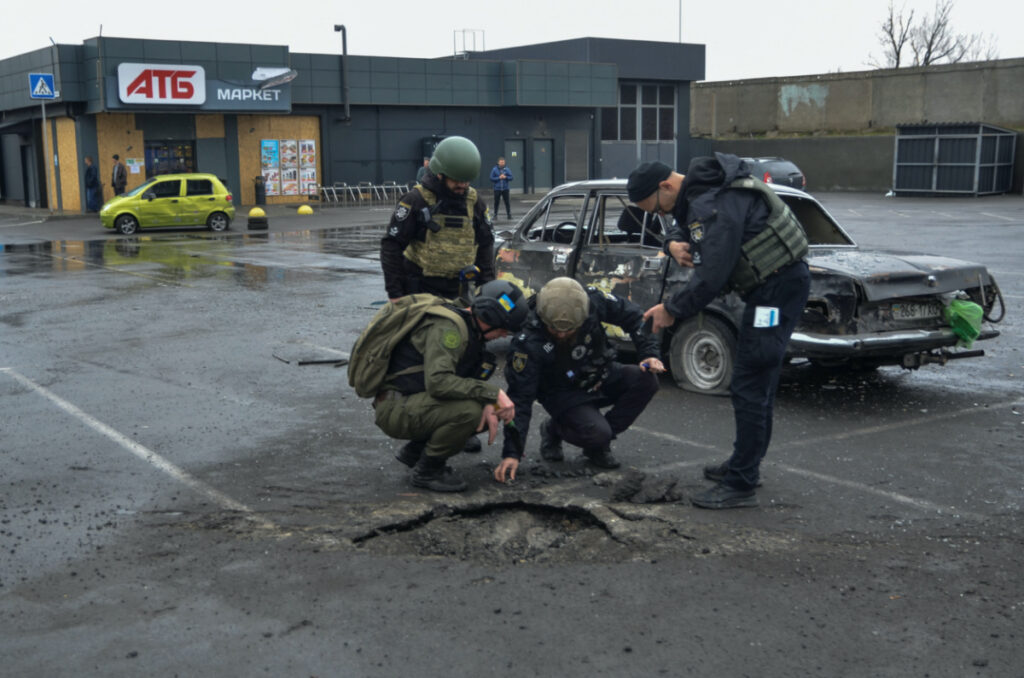 Police investigators inspect a shell crater left by a Russian military strike in a supermarket car park, amid Russia's attack on Ukraine, in Kherson, Ukraine March 11, 2023.