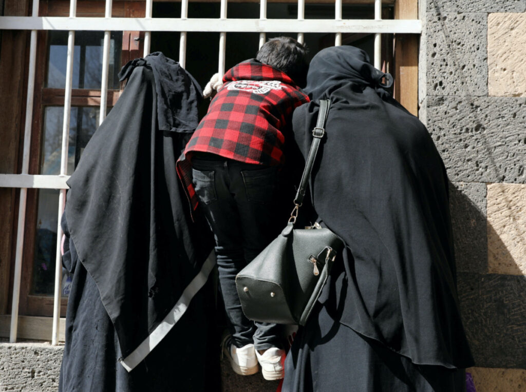 FILE PHOTO: Women and a boy wait for a foodstuff assistance vouchers at an aid distribution center in Sanaa, Yemen January 25, 2021. Picture taken January 25, 2021. REUTERS/Khaled Abdullah/File Photo
