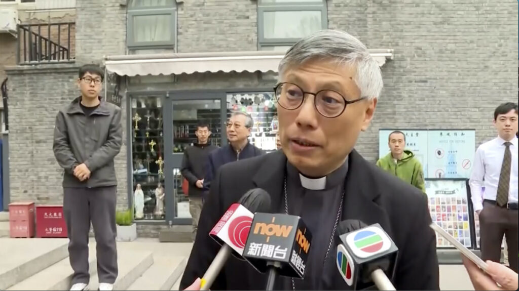 In this image from a video shot by Hong Kong broadcaster TVB, Hong Kong Bishop Stephen Chow talks to media during his visit to Beijing, with unidentified men standing behind him, on Thursday, 20th April, 2023.