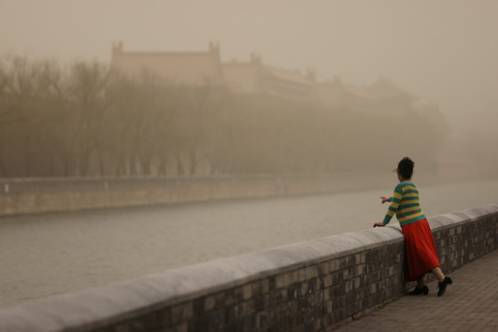 A woman poses for pictures near the Forbidden City, as the city is shrouded in smog amid a sandstorm, in Beijing, China, on 10th March, 2023.