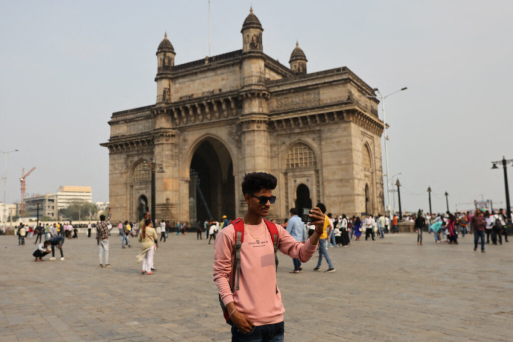A 21-year-old aspiring college student and migrant worker Sujeet Kumar shoots a video on his mobile phone in front of the Gateway of India monument in Mumbai, India, on 13th March, 2023.