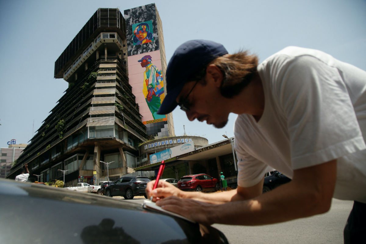 Fabio Lopez Gonzalo writes, in front of a mural by him and Elodie Arshak, who are known as Dourone, on a facade of the 'Pyramid', the emblematic tower of the Ivorian capital built in the 1970s and has fallen into disuse for twenty years, in Abidjan, Ivory Coast, on 19th April, 2023
