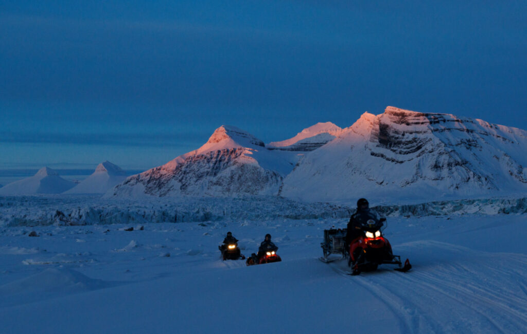 NPI scientists ride their snowmobiles as the sun sets at the banks of Kongsfjord and the Kronebreen glacier near Ny-Aalesund, Svalbard, Norway, on 10th April, 2023.
