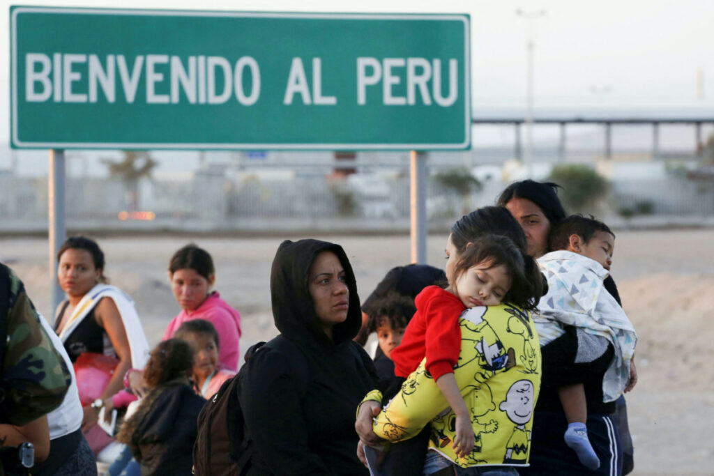 People stand next to a road sign reading 'Welcome to Peru' as undocumented migrants mostly from Venezuela, Colombia and Haiti remain stuck in Chile, after Peru refused to open its borders to migrants heading to their countries and Mexico, according to local media, in Chacalluta area, Arica, Chile, on 27th April, 2023