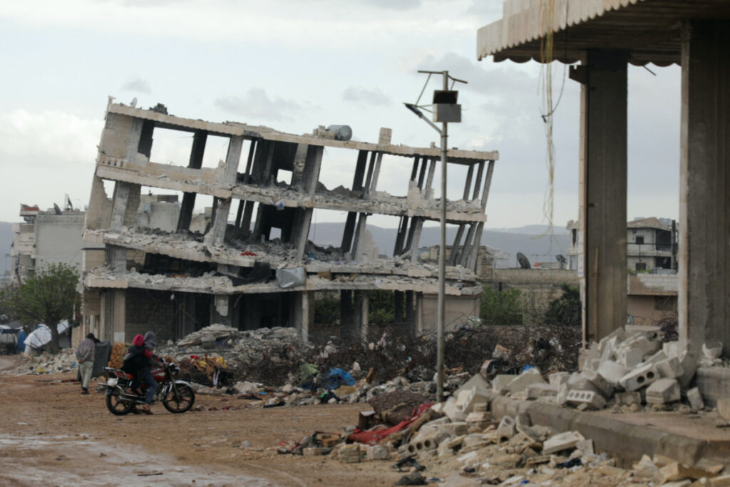 People ride a motorbike past buildings damaged by an earthquake that hit Syria on February 6, in the rebel-held town of Jandaris, Syria, on 29th March, 2023.