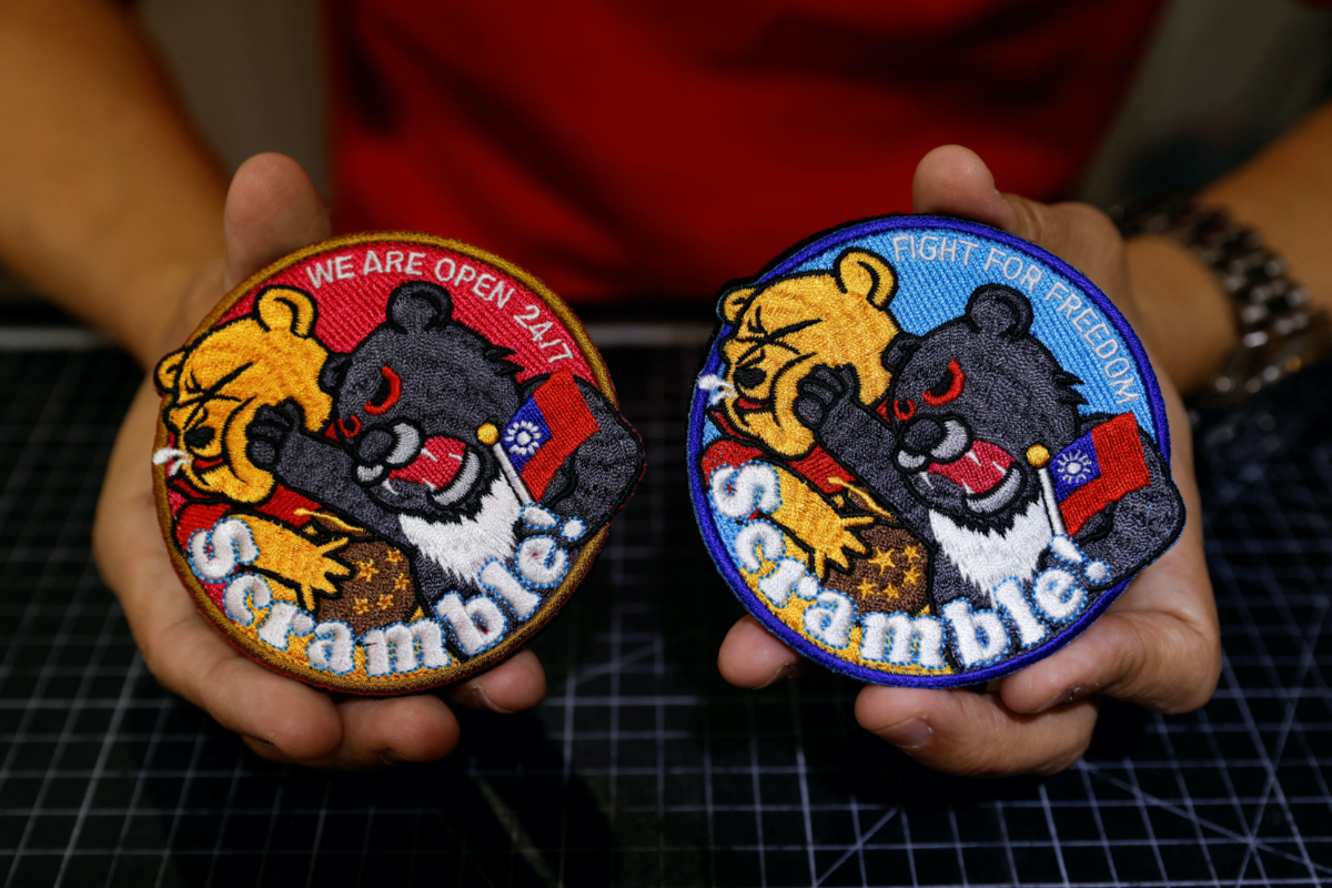 Alec Hsu shows to the camera patches depicting a Formosan black bear holding Taiwan’s flag and punching Winnie the Pooh at his store in Taoyuan, Taiwan, on 10th April 2023.
