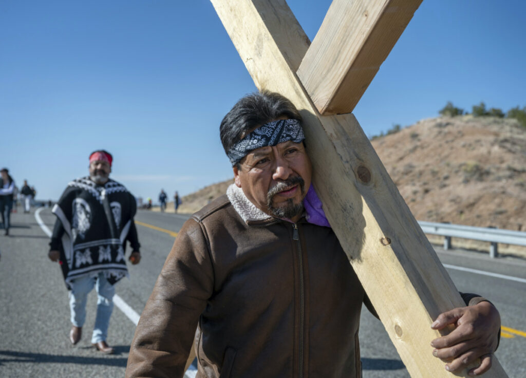 Jaime Gonzales, from Rio Rancho, and other family members carry a 68 kilogram cross along Santa Fe County Road 98 on their way to Santuario de Chimayo, Friday, 7th April, 2023