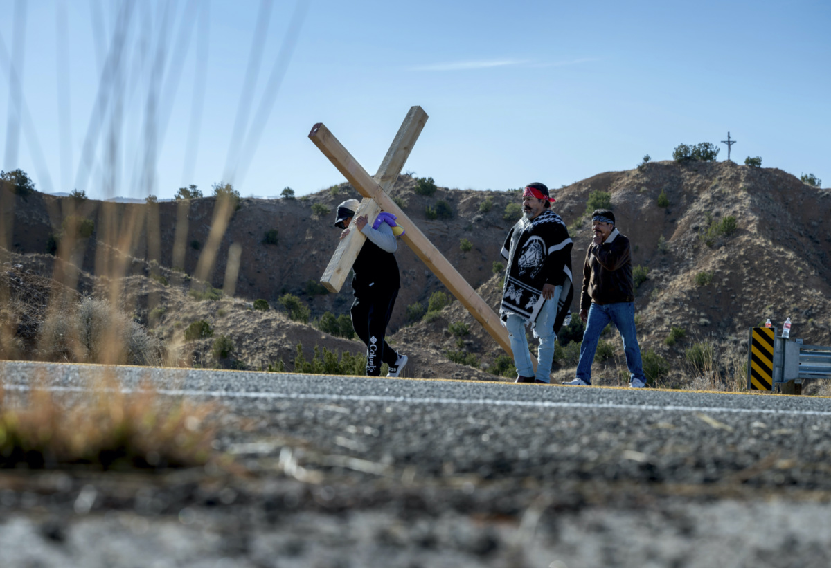 Javier Lopez, Raul Gonzales and Jaime Gonzales, from Rio Rancho, take turns carrying a 68 kilogram cross along Santa Fe County Road 98 on their way the Santuario de Chimayo, on Friday, 7th April, 2023.