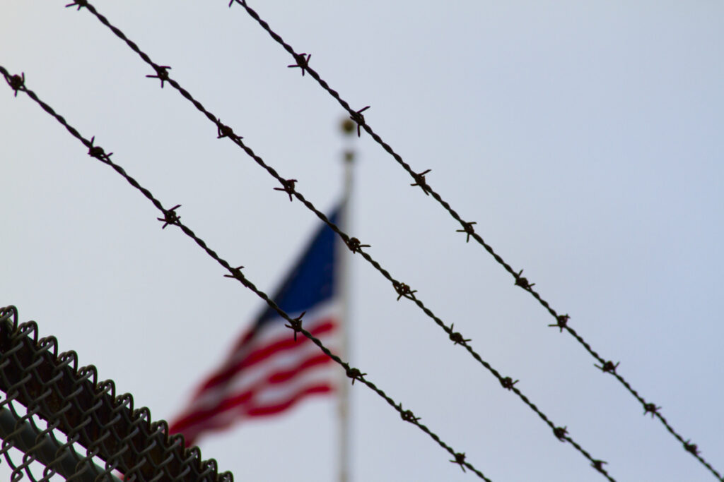 An American flag behind a barbwire fence.