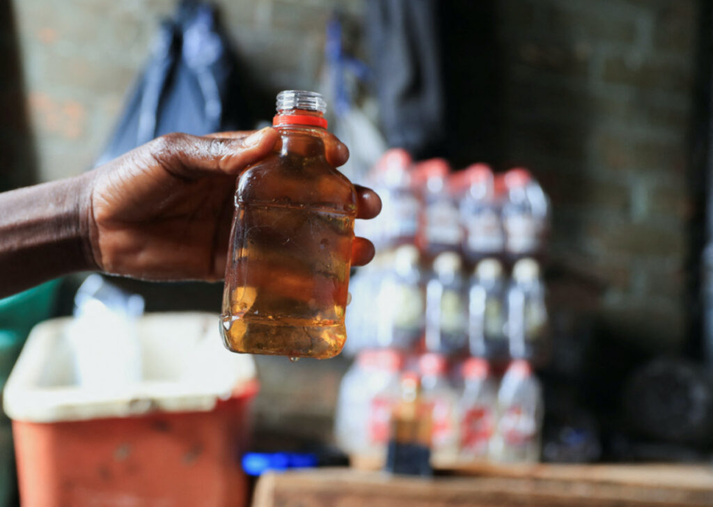 A person holds out a bottle at an informal brewing facility that makes fake whisky, brandy, vodka and other spirits, in Harare, Zimbabwe, on 23rd March, 2023