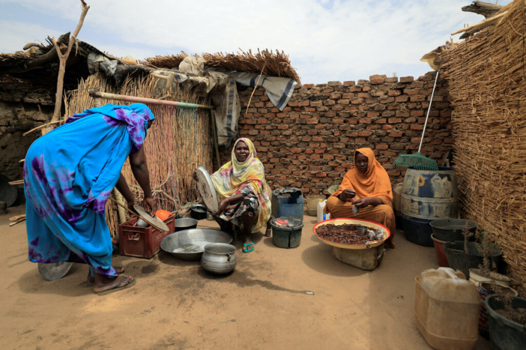 Fanna Hamit, 58, a Chadian widow who hosts in her compound a family of 11 Sudanese who fled the violence in Sudan's Darfur region, washes the dishes while Saboura Ahmed, 30, one of her Sudanese refugee guests, parcels roasted large crickets to sell as snacks, in the yard of her house near the border between Sudan and Chad in Koufroun, Chad, on 11th May, 2023.