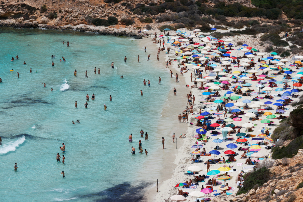 People sunbathe on the beach on the Sicilian island of Lampedusa, as a flow of migrants arriving on the Mediterranean island, in Lampedusa, Italy, on 22nd June, 2021
