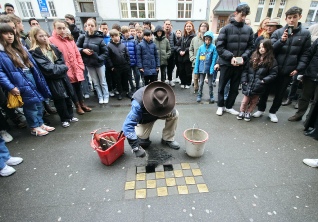 Stumbling stones artist Gunter Demnig is surrounded by relatives of Holocaust victims and pupils of the Deutzer Gymnasium Schaurtestrasse during a stone laying ceremony for a former teacher and a former pupil of the school in Cologne, Germany, on 8th March, 2023.