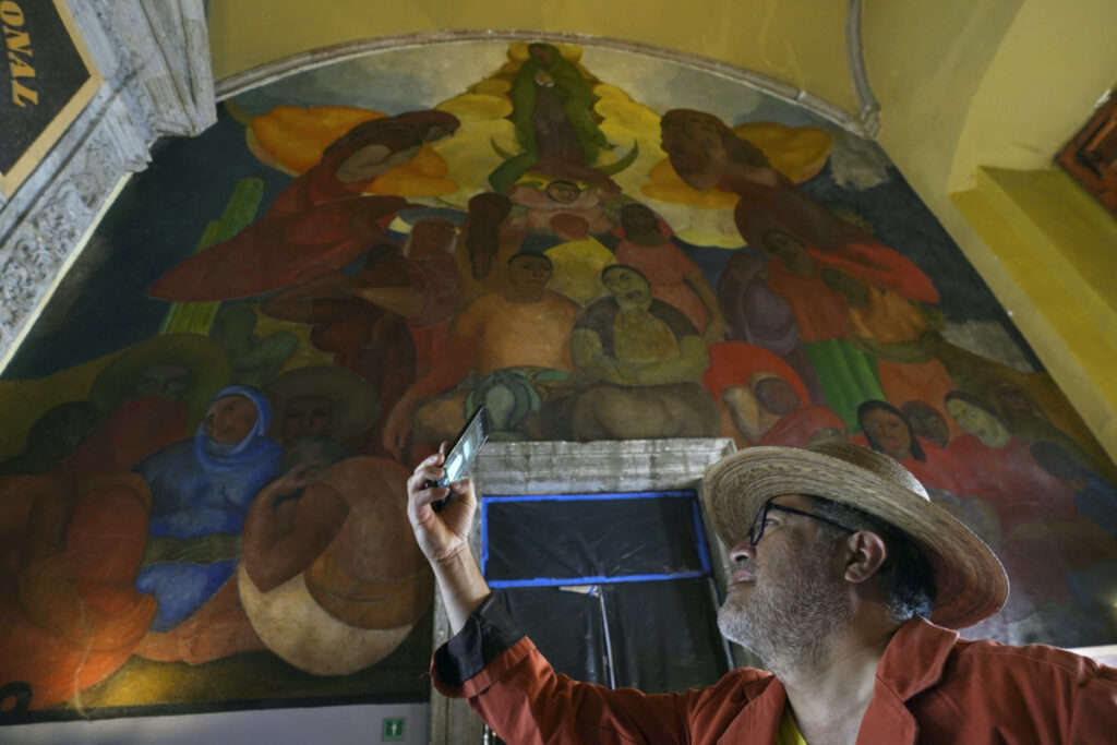 A tourist takes a photo backdropped by the "Alegoria de la Virgen de Guadalupe" mural, in the main entrance of the Antiguo Colegio de San Ildefonso, in Mexico City, on Wednesday, 26th April, 2023.