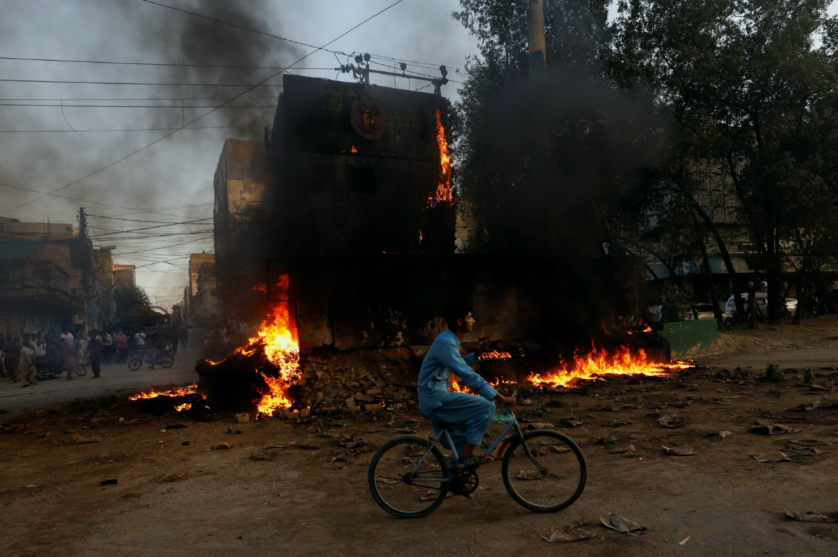 A boy rides past a paramilitary check post, that was set afire by the supporters of Pakistan's former Prime Minister Imran Khan, during a protest against his arrest, in Karachi, Pakistan, on 9th May, 2023.