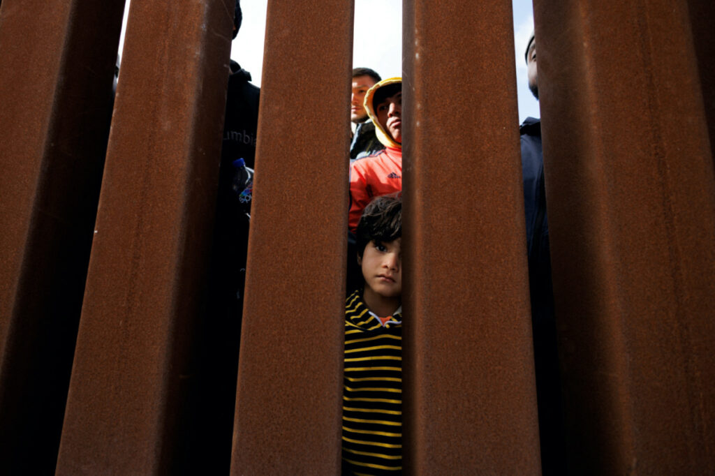A young boy peers through the border wall as migrants gather between primary and secondary border fences in San Diego as the United States prepares to lift COVID-19 restrictions that have blocked migrants at the US- Mexico border from seeking asylum since 2020 near San Diego, California, US, on 8th May, 2023.