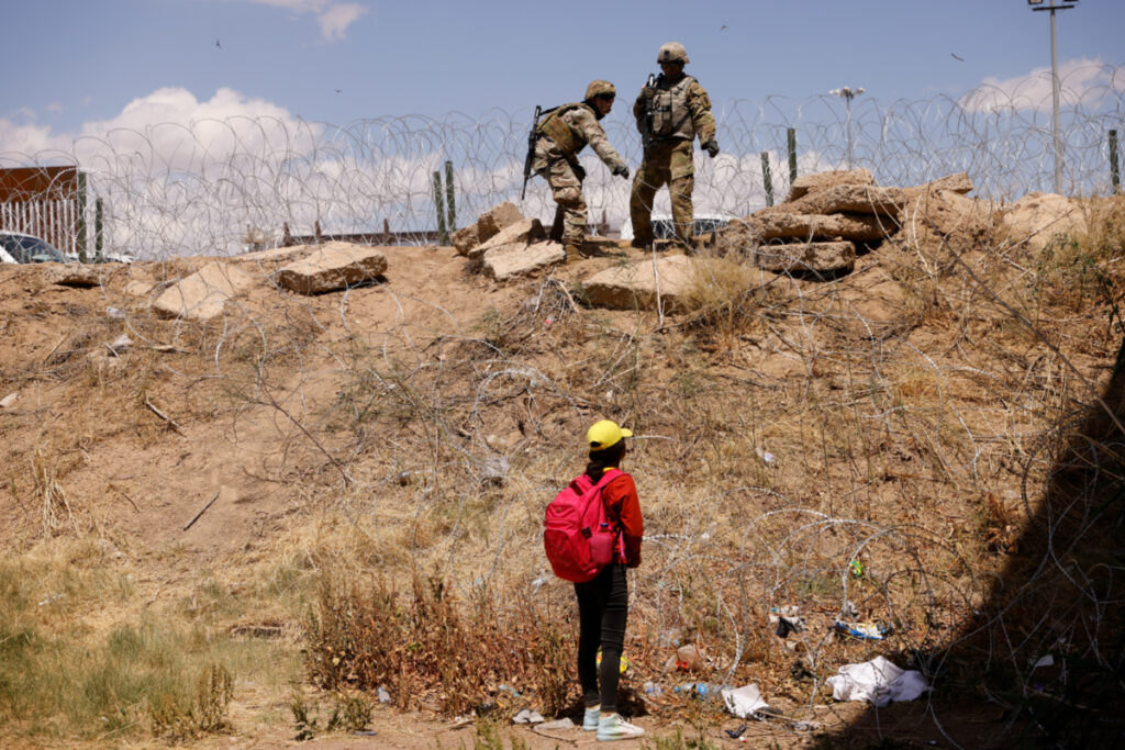 A young migrant, traveling alone from Guatemala, stands near the Rio Bravo river after crossing the border, to request asylum in the United States, as members of the Texas Army National Guard extend razor wire to inhibit migrants crossing, as seen from Ciudad Juarez, Mexico, on 13th May, 2023.