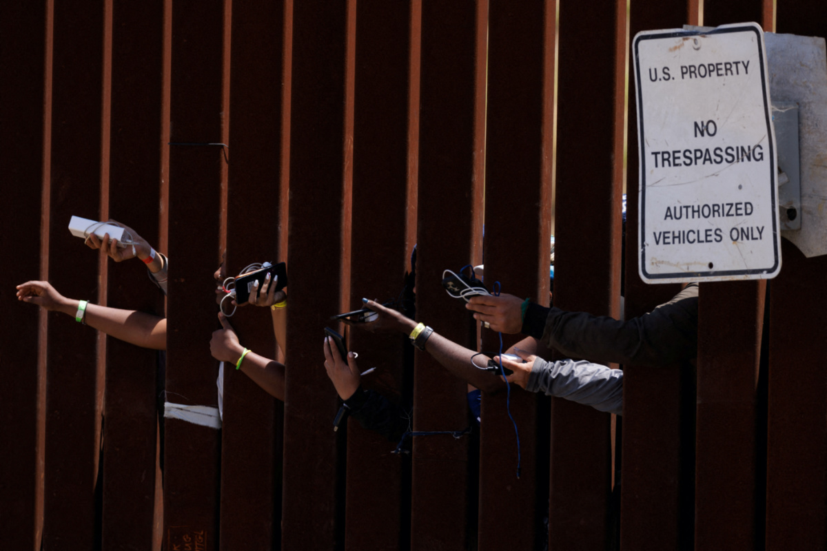 Migrants hope to get their phones charged by aid workers while they wait between the primary and secondary border fences as the United States prepares to lift COVID-19 era Title 42 restrictions that have blocked migrants at the US-Mexico border from seeking asylum since 2020, near San Diego, California, on 11th May, 2023