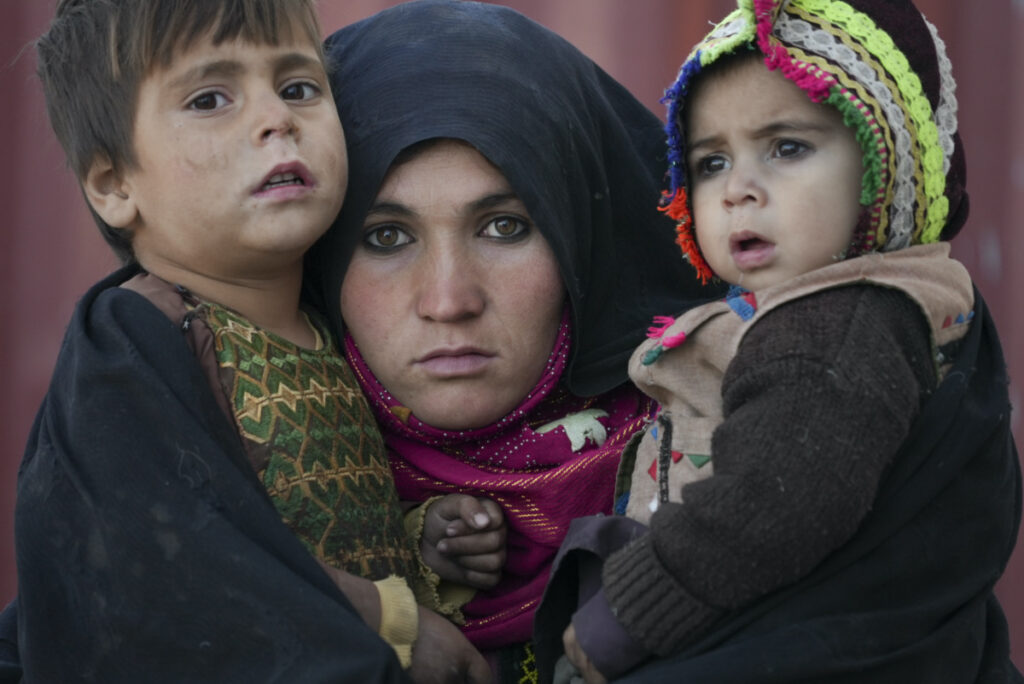 An Afghan woman holds her children as she waits for a consultation outside a makeshift clinic organized by World Vision in an IDP settlement near Herat, Afghanistan, on Thursday, 16th December, 2021.