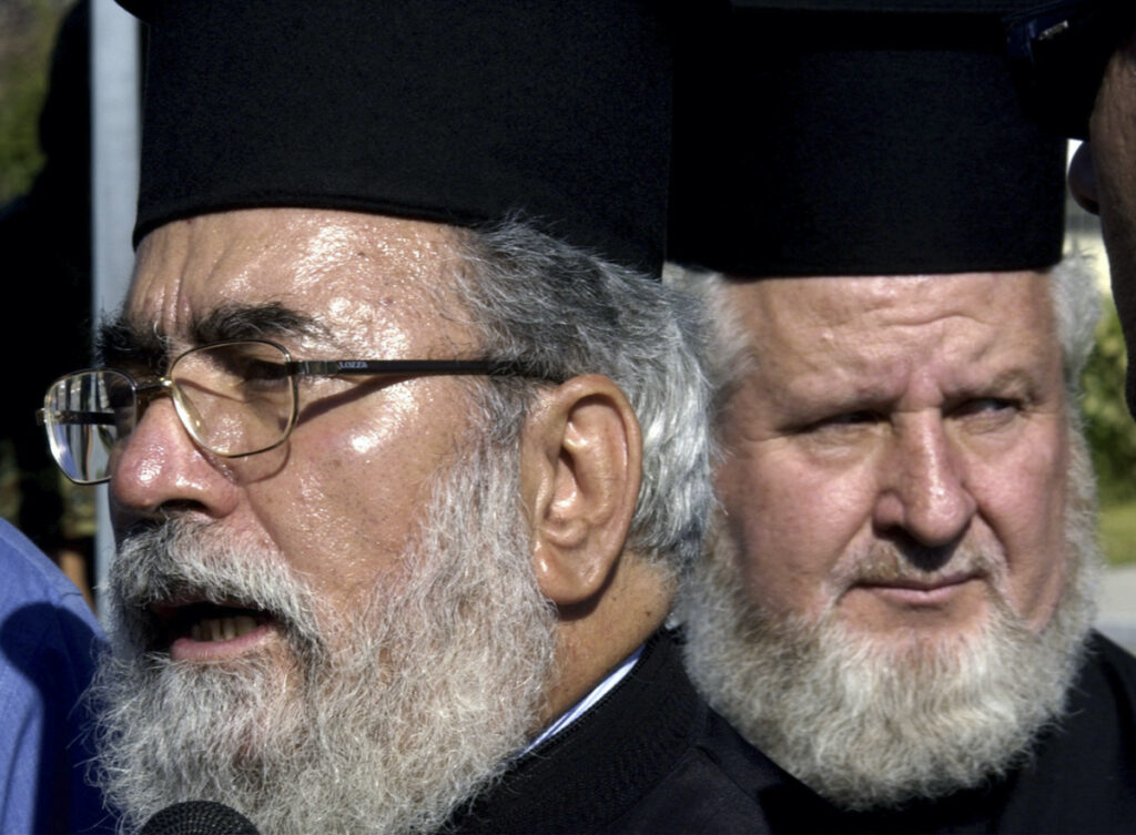 Bishop of Kition in Cyprus, Chrysostomos, left, flanked by an unidentified military priest, talks to reporters outside a military hospital in Athens on Sunday, 12th September, 2004.