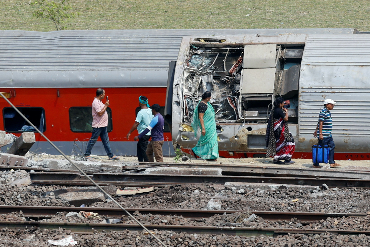 People walk past a damaged coach at the site of a train collision following the accident in Balasore district in the eastern state of Odisha, India, on 4th June, 2023
