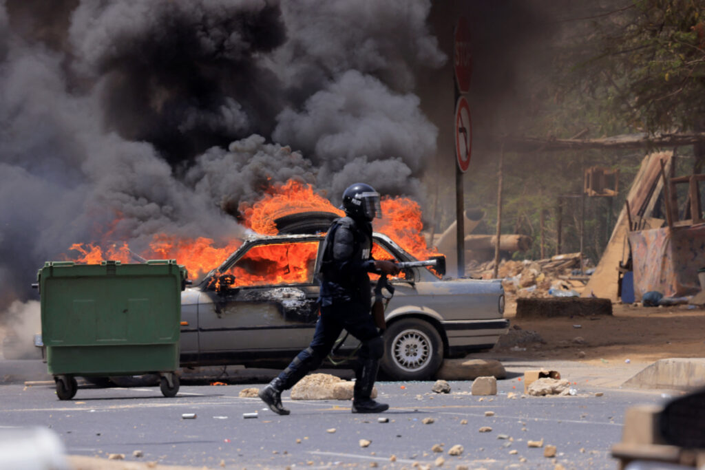 A riot police officer walks near a car set on fire during clashes between supporters of Senegalese opposition leader Ousmane Sonko and security forces after Sonko was sentenced to prison in Dakar Senegal, on 1st June, 2023