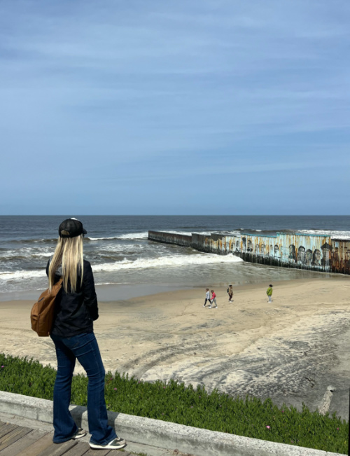 Bri Stensrud looks out over the border wall stretching off the beach and into the water. 