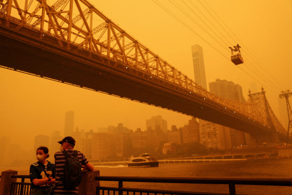 People wear protective masks as the Roosevelt Island Tram crosses the East River while haze and smoke from the Canadian wildfires shroud the Manhattan skyline, on 7th June, 2023