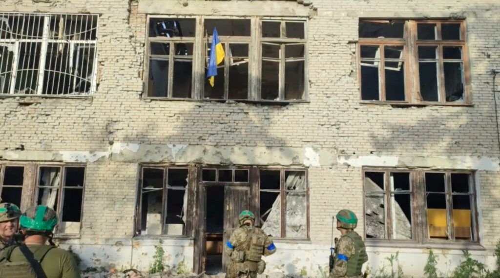Ukrainian soldiers stand in front of a building with a Ukrainian flag on it, during an operation that claims to liberate the first village amid a counter-offensive, in a location given as Blahodatne, Donetsk Region, Ukraine, in this screengrab taken from a handout video released on 11th June, 2023.