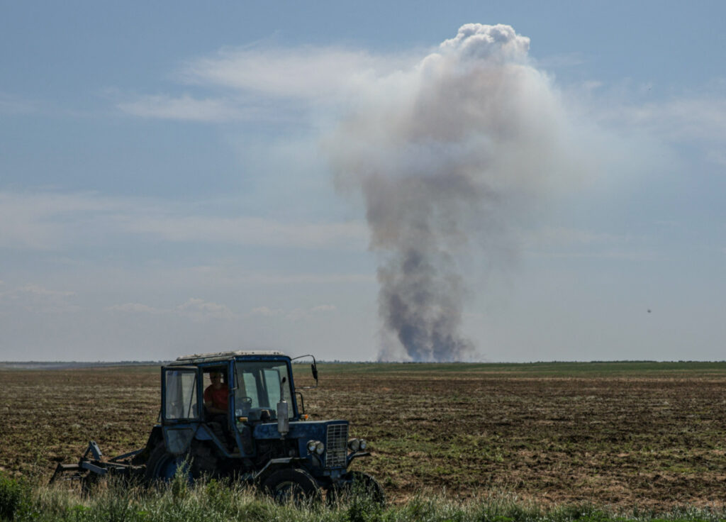 An agricultural worker operates a tractor as smoke rises in the distance after a military strike, in Kherson region, Ukraine, on 20th June, 2023.